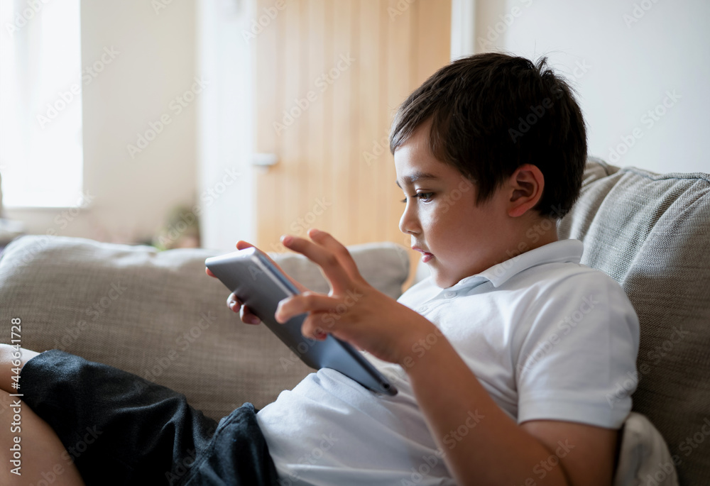 School boy using tablet studying online on internet, Kid playing game or watching cartoon on digital pad, Happy Child relaxing at home, Children with technology and social network concept School boy using tablet studying online on internet, Kid playing game or watching cartoon on digital pad, Happy Child relaxing at home, Children with technology and social network concept
