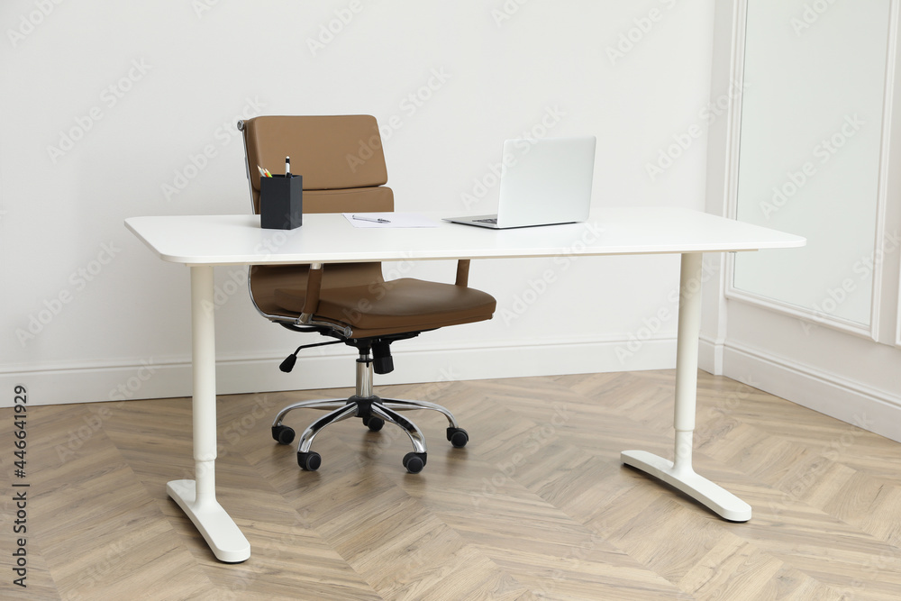 Stylish workplace with laptop and comfortable armchair near white wall indoors. Interior design Stylish workplace with laptop and comfortable armchair near white wall indoors. Interior design