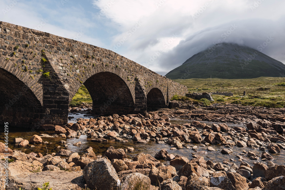 Old vintage brick bridge crossing river in Sligachan, Isle of Skye, Scotland with scottish landscape, vegetation, hills and mountains with fresh, blue water and sunny sky
