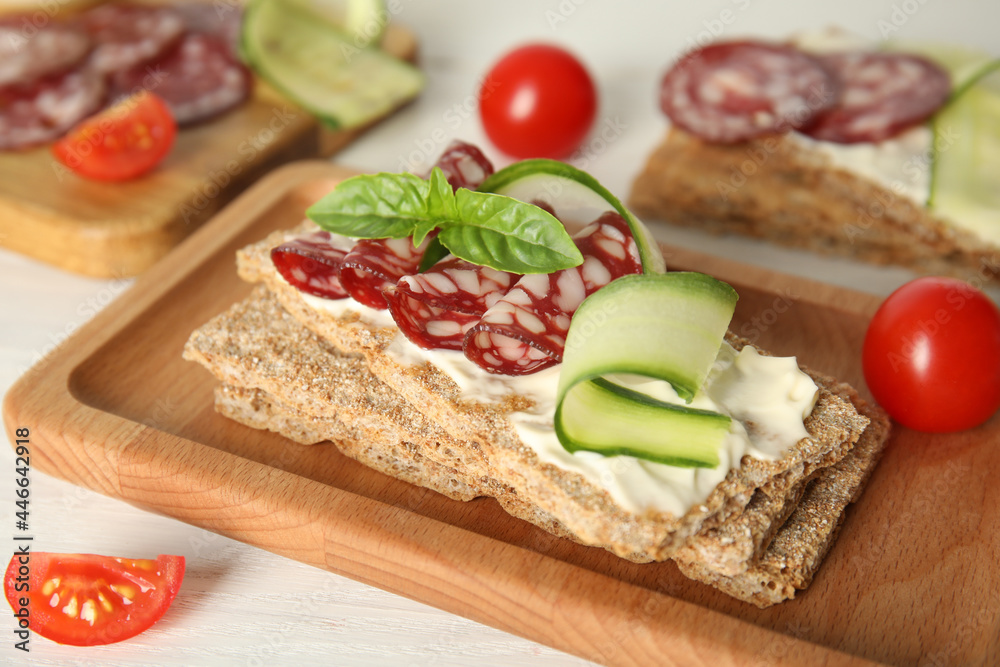Fresh rye crispbreads with salami, cream cheese and cucumber on white wooden table, closeup