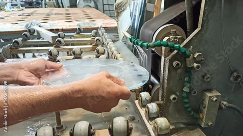 Worker hands grind glass on a machine. Jets of water cooling machine processing of glass. Glass blank working on grinding machine. Cooling of heating parts during glass working. Industrial concept
