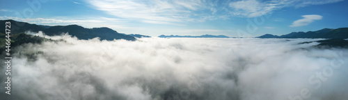 Sea of clouds in mountains. Scenic panorama with blue sky and overcast layer of clouds in mountain valley viewed from above