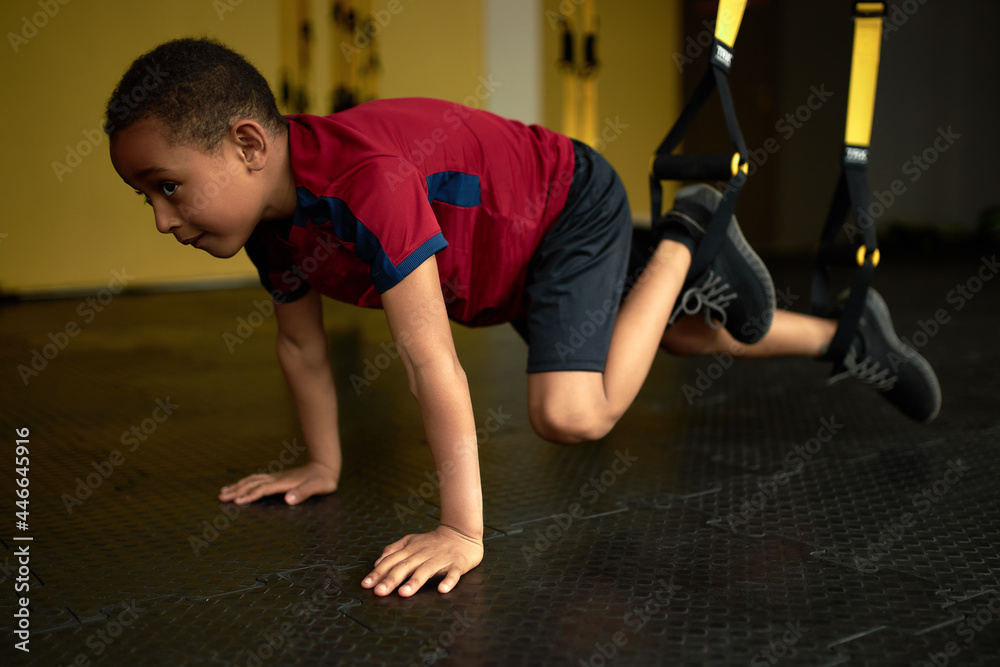 Fototapeta premium Latino american kid performing difficult exercise on machine in gym. Train strength and endurance from childhood. Sport, hobby, exercise, gymnast, health, training, athlete concept