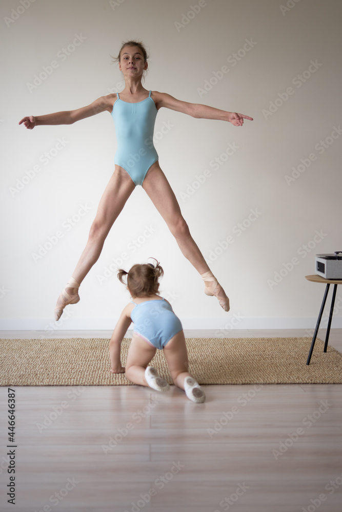  two girls the older ballerina in a jump the younger one crawls on her knees in the hall under the record in blue swimsuits        