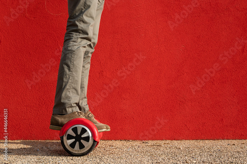 Unrecognizable man riding red mini hoverboard. Red wall on background photo