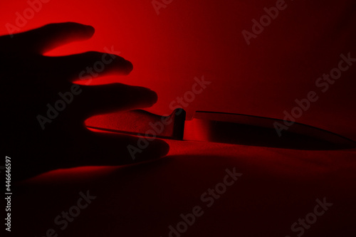Silhouetted hand reaching for knife bathed in red light
