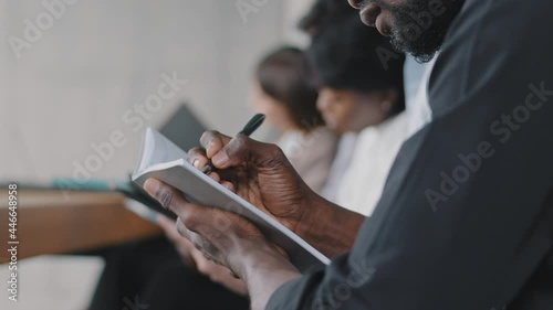 Close-up male hands with dark skin write in notebook use pen ideas plans notes strategy, unknown african black ethnic business man afro guy writing sitting at office meeting training with colleagues photo