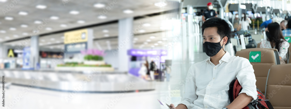 Asian businessman in airport terminal, wears medical mask during covid-19 or coronavirus crisis.