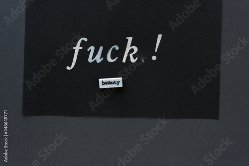 the words "fuck" in alpha/numeric plastic stencil letter type - hand painted in white acrylic paint - on black pad paper with faint lines and the word beauty - on dark gray paper