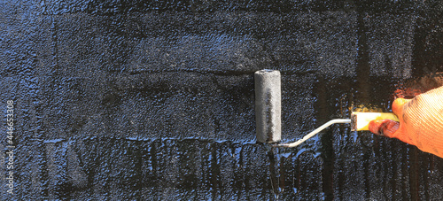Obraz na plátně Roofer paints the surface of asphalt bitumen with a roller brush