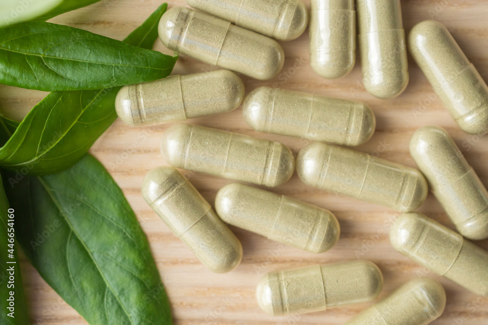 Herbal medicine capsules with Andrographis paniculata leaf on wood table Herbal medicine capsules with Andrographis paniculata leaf on wood table
