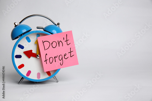 Alarm clock and reminder note with text Don't forget on light grey background. Space for design photo