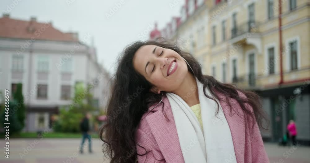 Happy cheerful girl with curls stands in the middle of the city street looks at the camera smiles loves life shows her good mood for happy emotions Happy cheerful girl with curls stands in the middle of the city street looks at the camera smiles loves life shows her good mood for happy emotions