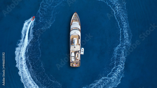 Aerial drone top down photo of stunt man performing extreme stunts and circling with jet ski watercraft over anchored yacht in deep blue ocean sea