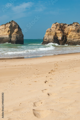 Close-up of the footprints in the sand of an empty beach, cliffs in the ocean in the background, blue sky