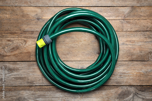 Green garden hose on wooden table, top view