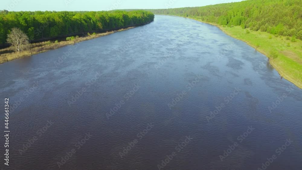 Wide river, green grass on the bank, forest, aerial view. Ripples on the surface of the water. Beautiful background, natural landscape with a calm stream of water at sunset. UHD 4K. Wide river, green grass on the bank, forest, aerial view. Ripples on the surface of the water. Beautiful background, natural landscape with a calm stream of water at sunset. UHD 4K.