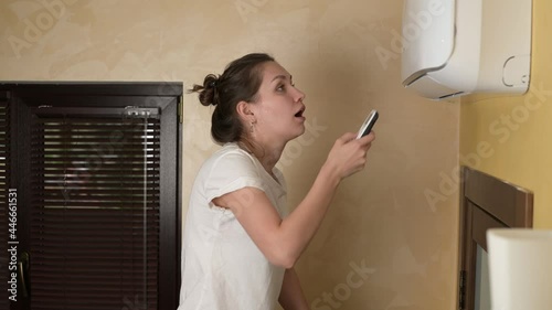A young woman turns on the air conditioner at home on a hot summer day and enjoys the coolness