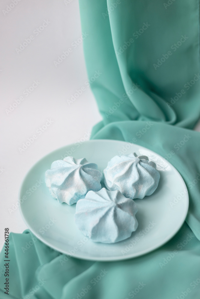 Three meringue cookies on the light blue plate with textile background Three meringue cookies on the light blue plate with textile background