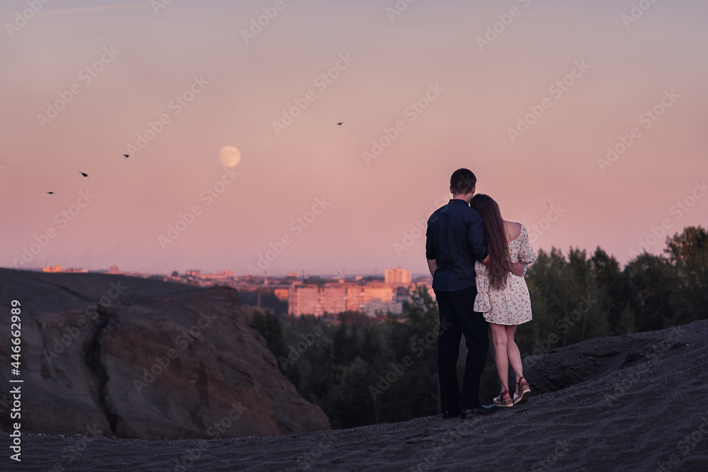 Loving couple embracing and looking moon and city oin sunset