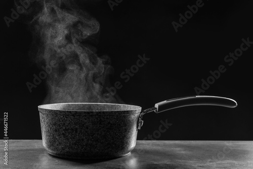 Steaming saucepan on grey table against dark background