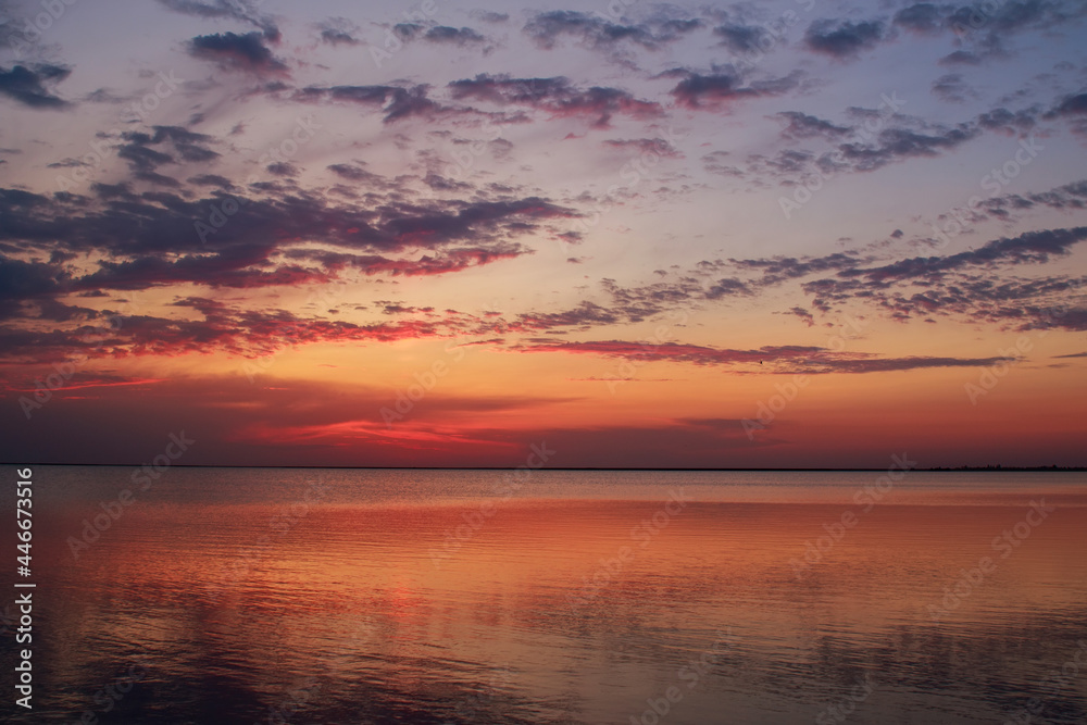 Dreamy and dramatic colorful sunset sky over calm water surface with cloud reflections