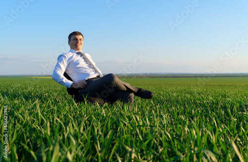 businessman sits in an office chair in a field and rests, freelance and business concept, green grass and blue sky as background © soleg