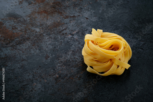 Natural Raw pasta tagliatelle on a black stone background. Fresh uncooked egg Italian pasta, copy space