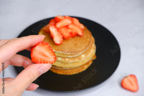 Girl holding strawberries in her hands on a blurred background. Pancakes with strawberries on a blurred background. Photo of food.