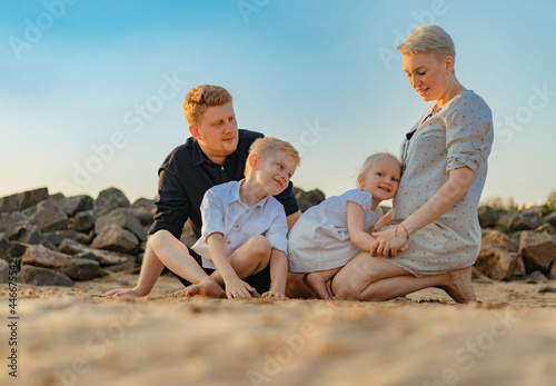 happy caucasian family expecting baby. girl touching mom's belly. Loving son and husband looking tender. enjoy sunset on beach