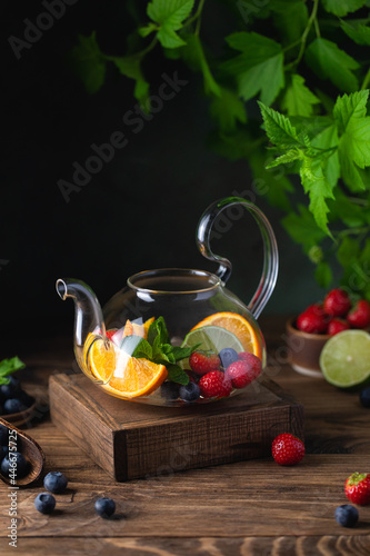 Fruit red tea with berries in glass teapot on wooden background