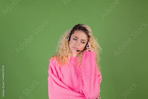 Young blonde woman with long curly hair in pink sweater on green background call centre worker manager bored tired disappointed listen client © Анастасия Каргаполов