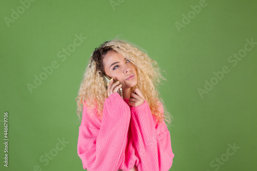 Woman in pink sweater on green background holding mobile phone thoughtful