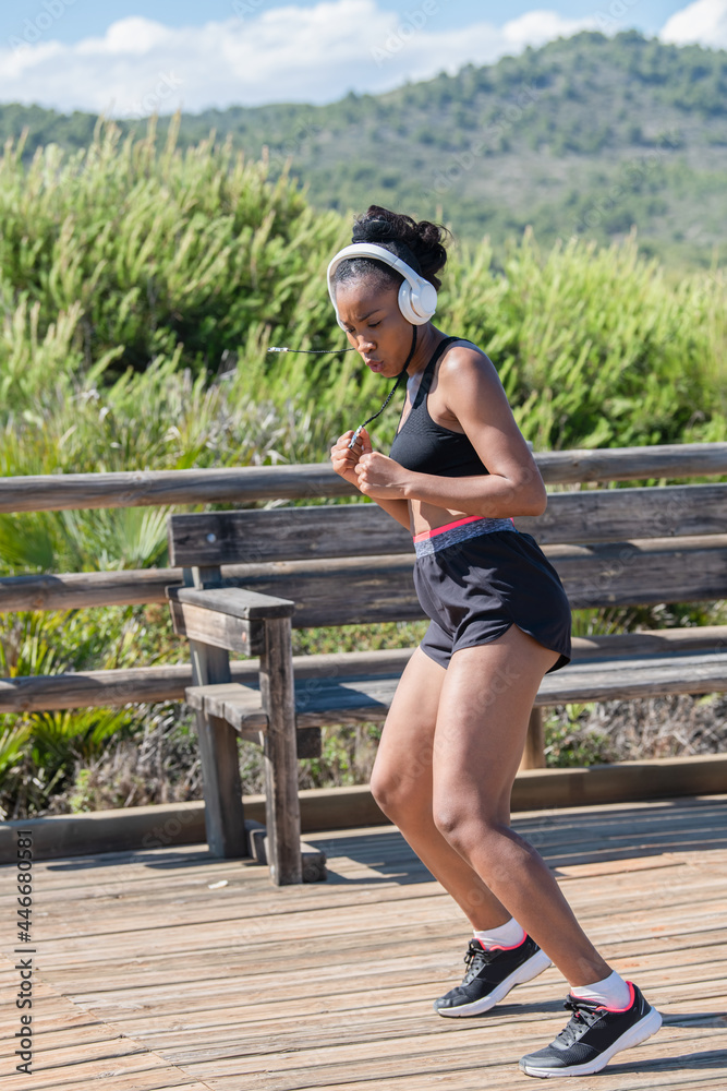 Tough afro american woman with headphones exercising outdoors: Exercise and strength concept.
