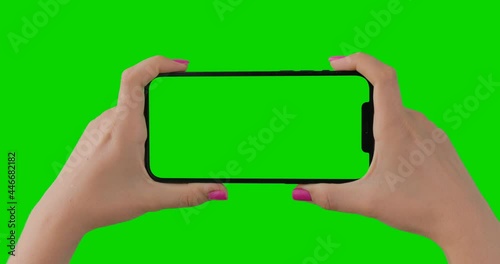 Close up of woman hands with pink manicure holding horizontal smartphone with green screen. Isolated chroma key mobile Apple iPhone 12 Pro Max perfect for product placement.