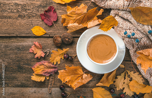 A cappuccino cup, a sweater and autumn foliage on a wooden background. Festive autumn background. Space for copying.