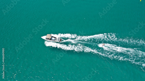 Aerial drone photo of woman practicing high speed water ski towed by large speed boat in emerald tropical lake © aerial-drone