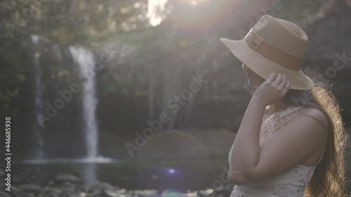 Mid shot of a young woman in a floral dress standing in front of a waterfall smiling