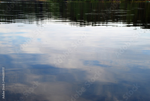 Reflection of the sky and clouds from the water surface. The almost flat surface of clear water reflects blue skies and white fluffy clouds and forest, giving the water a mysterious look.