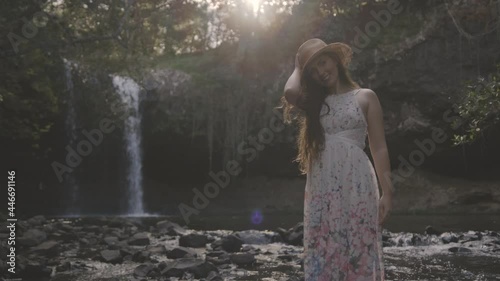 Young woman in a floral dress standing in front of a waterfall