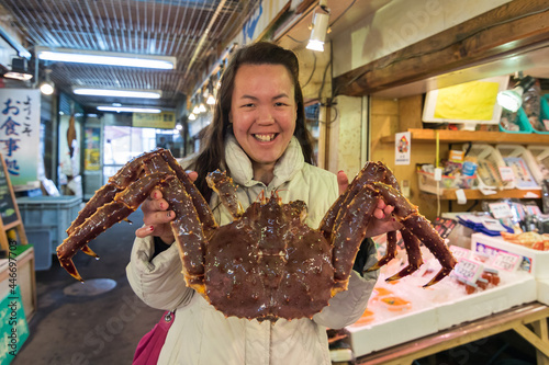 Pretty Young Asia Tourist girl holding huge and the most famous food King Crab fresh seafood market SANKAKU MARKET , Otaru, Hokkaido, Japan photo