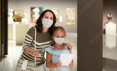 Mother and daughter in protective masks with guide enjoying expositions in museum