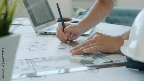 Close-up of female hands drawing on blueprint while architect is working at home using laptop. Contemporary activities and professions concept.