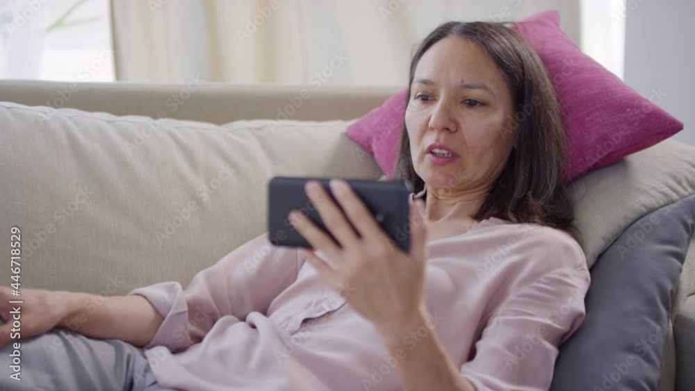 Portrait of modern mature woman spending time at home during lockdown relaxing on sofa having video call with physician on smartphone Portrait of modern mature woman spending time at home during lockdown relaxing on sofa having video call with physician on smartphone