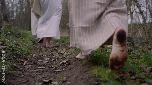 Three ancient women in traditional clothing walk barefoot through the forest, backview - focus on the feets