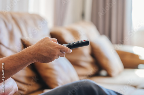 TV remote control in hand of man sitting on sofa in living room