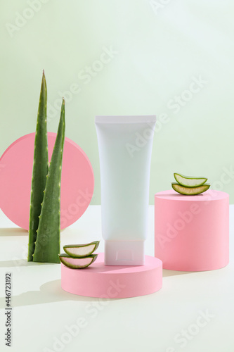 Green Background with natural cosmetics of aloe vera, fresh leaves of aloe on bright green and podium geometrical pink. Blank white cosmetic skincare makeup containers photo