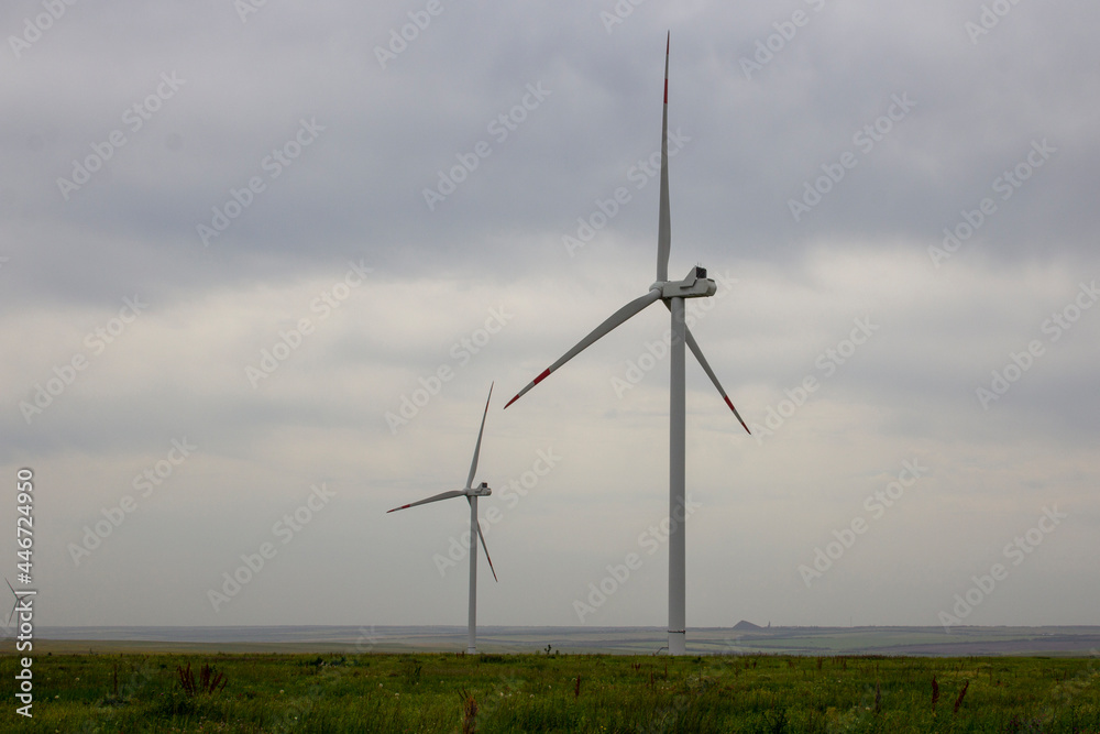 Industrial wind turbines are on the plain. Huge windmills stand on the plain under a gloomy sky. Industrial wind turbines are on the plain. Huge windmills stand on the plain under a gloomy sky.