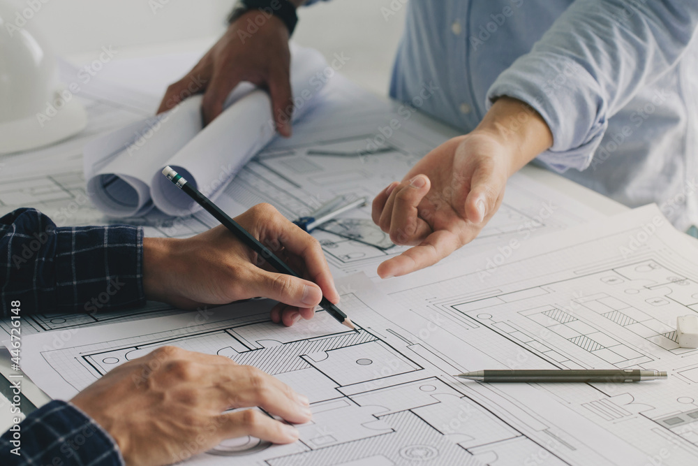 Fototapeta Two business man construction site engineers. working drawing on blueprint and discussing the floor plans over blueprint architectural plans at table in a modern office. construction concept
