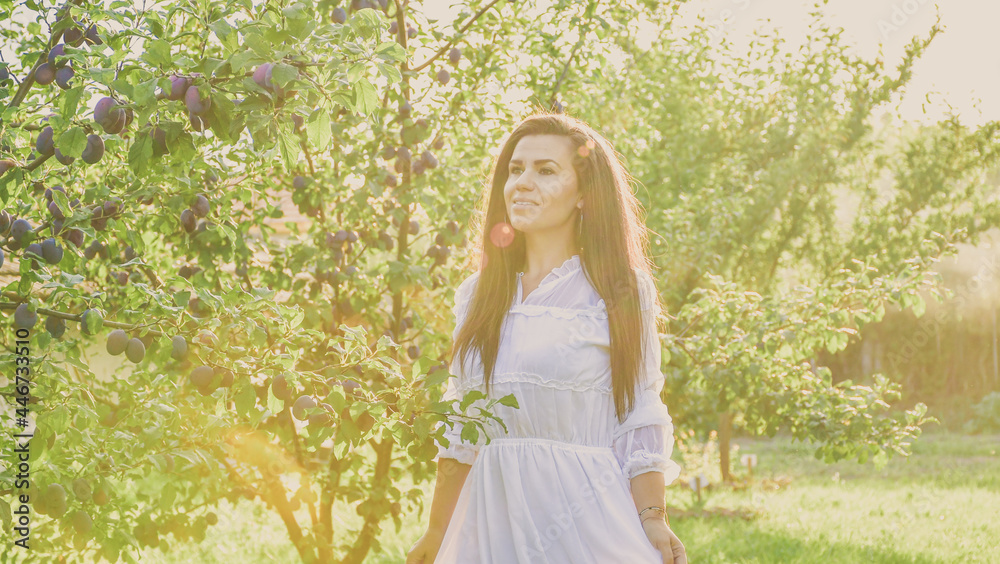 Young beautiful smiling woman with romantic dress at orchar near a plum tree. Young pretty farmer woman Young beautiful smiling woman with romantic dress at orchar near a plum tree. Young pretty farmer woman